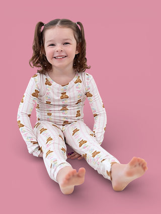 Young child wearing long-sleeve white pajamas with brown bear and floral print pattern against pink background.