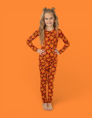 Child wearing orange long-sleeve pajama set with basketball print pattern.