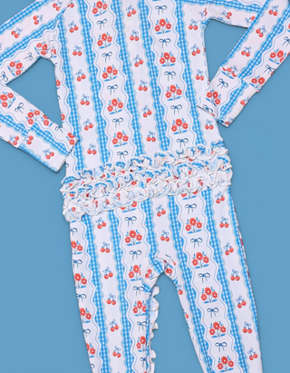 White romper with red floral and cherry print, blue gingham stripes, and ruffled waist and leg trim.