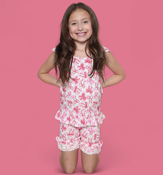 Girl's sleeveless top and shorts set with pink bow print and ruffled trim on white background.
