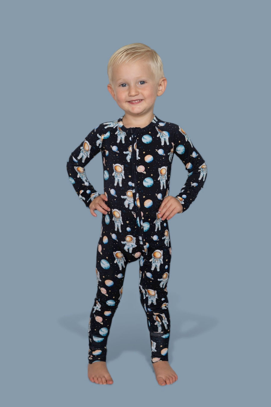 Toddler wearing black long-sleeve romper with astronaut and planet print throughout.