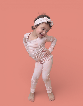 Young child wearing cream-colored long-sleeved top and matching leggings with white bow headband.