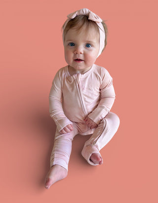 Infant wearing pink long-sleeve zippered romper with matching bow headband on coral background.