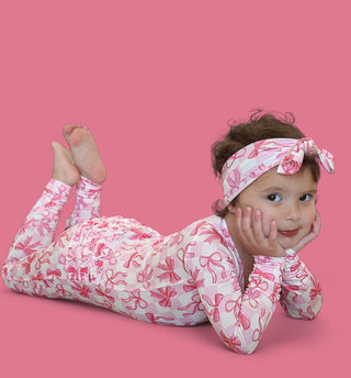 Infant wearing pink and white checkered romper with bow pattern and matching headband against pink background.