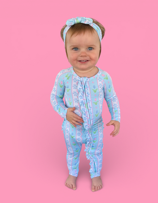 Toddler wearing light blue long-sleeve romper with tulip and floral pattern, front zipper, and matching headband.