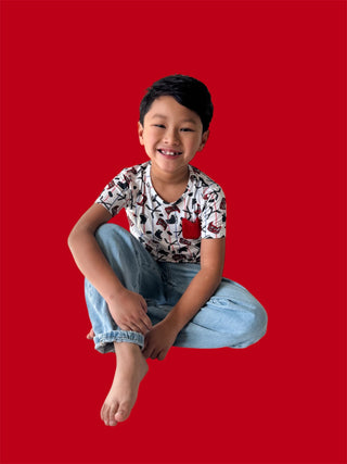 Child wearing cream pocket tee with black and red hockey stick print and light blue jeans against red background.