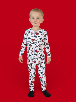 Young child wearing long-sleeve pajama set with hockey stick and skate print on cream background, paired with black socks.