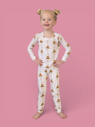 Young child wearing white long-sleeve pajamas with brown teddy bears and floral pattern throughout.