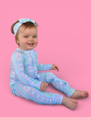 Toddler wearing light blue romper with pink and green tulip print and matching headband.