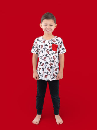 Boy wearing white short-sleeve tee with red pocket and hockey/skateboard print, paired with black pants.