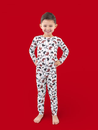 Young child wearing white long-sleeve pajamas with red and black hockey stick and skate pattern against red background.