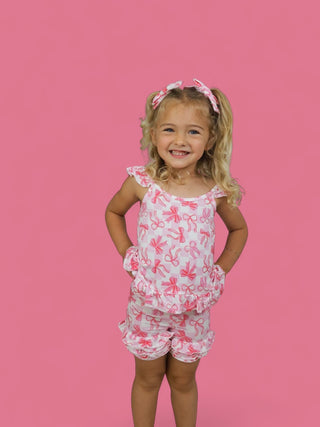 Girl wearing white shorts with pink bow pattern and ruffled legs, matching sleeveless top with ruffle trim.