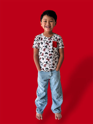 Child wearing white short-sleeve tee with red and black skate and stick graphics and chest pocket, paired with light blue jea