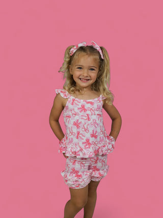 Toddler wearing pink and white bow-print shorts with ruffled hem and matching ruffle-trimmed tank top.