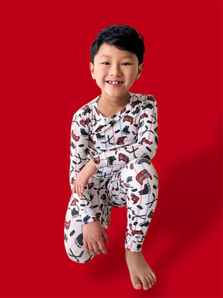 Child wearing white pajamas with black and red hockey stick and skate print pattern against red background.