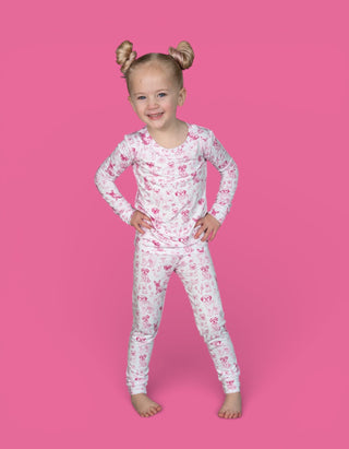 Young child wearing a two-piece pink and white puppy print pajama set with long sleeves and pants against a pink background.
