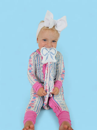 Small child holding white plush lovey with blue bow design against light blue background.