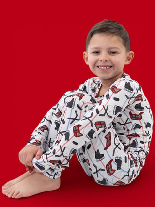 Young boy wearing white pajama shirt with hockey stick and skate print pattern against red background.