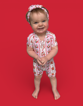 Toddler wearing white shortie pajamas with red berry and bear print, matching headband, against red background.
