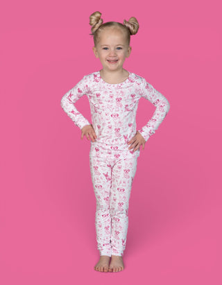 Young child wearing white long-sleeve pajama top and pants with pink puppy toile pattern against pink background.