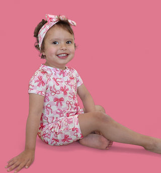 Toddler wearing white short-sleeve romper with pink bow print and matching bow headband.
