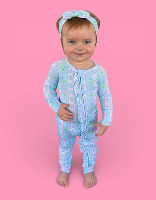 Toddler wearing light blue long-sleeve romper with tulip and floral print, matching headband with bow detail.