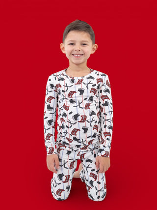 Young child wearing long-sleeve white pajama set with red and black hockey stick and skate pattern.