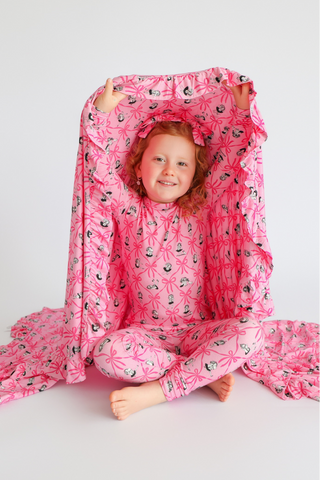 Pink ruffle blanket with bow and character print, draped over child.