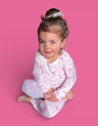 Toddler wearing white long-sleeve pajamas with pink puppy toile print, seated against pink background.