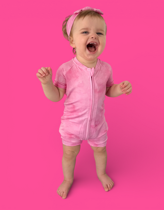 Toddler wearing pink short-sleeve romper with front zipper and matching pink headband against bright pink background.