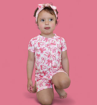 Toddler wearing pink and white short-sleeved romper with bow print and matching headband.