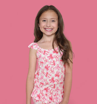 Girl wearing pink and white bow-print tank top with ruffled short sleeves against pink background.