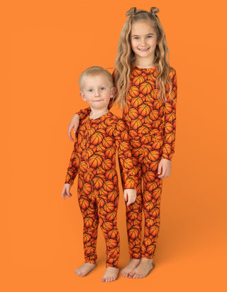 Two children wearing orange pajamas with basketball print pattern on orange background.