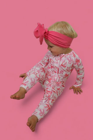 Infant romper with pink and white bow print, long sleeves, and front zipper, displayed with matching pink bow headband.