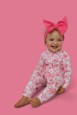 Toddler wearing pink bow headband and white romper with pink bow print and long sleeves.
