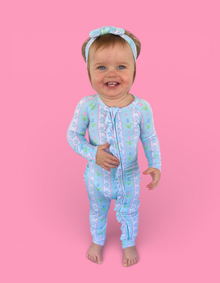 Toddler wearing light blue long-sleeve romper with tulip and geometric pattern, matching headband, front zipper closure.