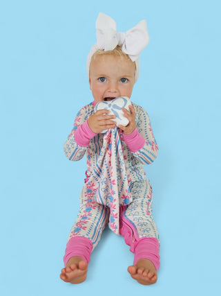 Infant holding white plush lovey with blue pattern against blue background.